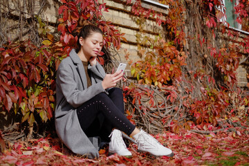 Wall Mural - young beautiful brunette girl of European appearance is sitting in an autumn Park and talking on a mobile phone