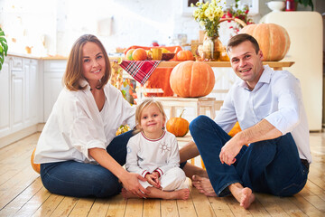 Wall Mural - A happy family of three, mother, father and daughter, stand on a light kitchen, a wooden table with an autumn harvest - pumpkins, apples