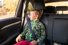 Little Boy Sitting On A Booster Seat Buckled Up In The Car.