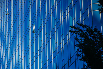 Glass office building in a city. Two windows open to let fresh air in. Business office glass building reflects blue sky.