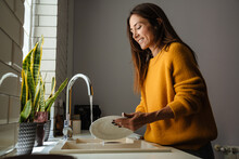 Beautiful Middle-aged Woman Smiling While Washing Dishes At Home