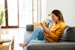 © Drobot Dean - Beautiful woman smiling and using cellphone on sofa in apartment