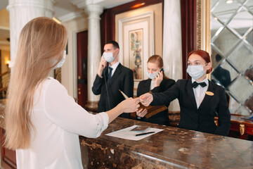 Check in hotel. receptionist at counter in hotel wearing medical masks as precaution against virus. Young woman on a business trip doing check-in at the hotel