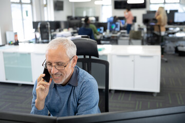 Senior businessman talking on smartphone while sitting on his desk at modern office