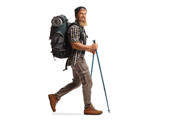 full length profile shot of a bearded guy hiker with a backpack and hiking poles walking