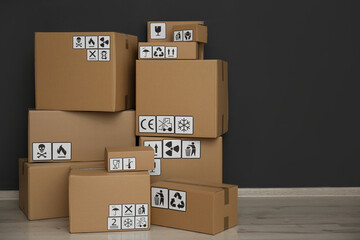 Wall Mural - Cardboard boxes with different packaging symbols on floor near black wall. Parcel delivery