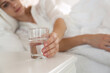 © New Africa - Woman taking glass of water from nightstand in bedroom, closeup