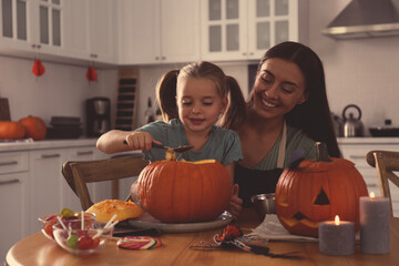 Canvas Print - Mother and daughter making pumpkin jack o'lantern at table in kitchen. Halloween celebration