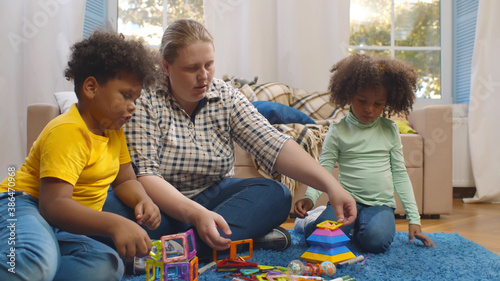 Young caucasian mother enjoying playing with mixed race son and daughter indoors.