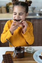 A Little Girl Holds Chocolate, Toast Bread With Chocolate Paste. Happy Baby Has Breakfast In The Kitchen Favorite Sweets