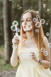 © Suzana - blonde woman in a yellow dress blowing bubbles with trees in a blurry background