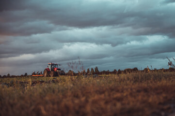 Wall Mural - Tractor plowing the fields in the countryside by sunset. Agricultural tractor plowing the field. Red Tractor with plow. Sunset over the autumn field.