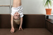 Boy is upside down over sofa. Funny child hangs upside down.