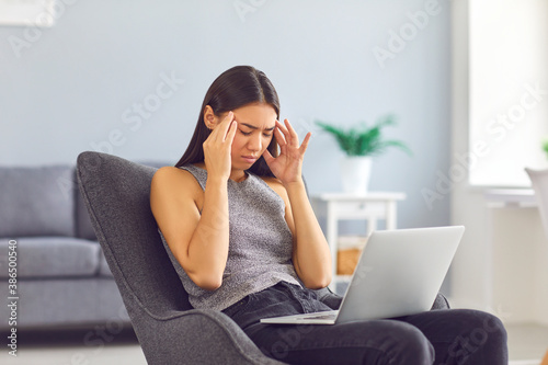 Fotografía Tired young woman rubbing temples suffering from headache sitting in armchair wi
