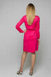 Full length stock photo of unrecognizable model posing in bright pink dress with belt and fashionable heels with rhinestones in studio. Back view of blonde model in dress with hand on waist.