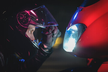 Wall Mural - A motorbiker with open helmet visor is looking on his motorbike close up.