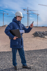 Wall Mural - A construction worker in a white helmet with a laptop and documents under his arm is talking on the phone