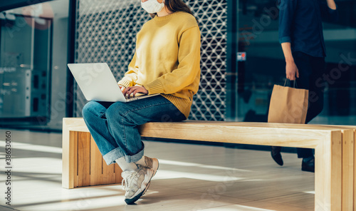 Plakat young woman is working on a laptop while sitting outside a city building