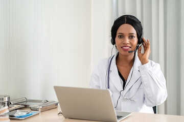 african woman doctor in headset taking calling on her headset microphone online for a ache patient