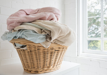 Close up of pink towel and blue sheets in wicker washing basket on shelf next to window (selective focus)