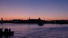 Blue Hour Stationary Footage Of A Harbor At Sunset A Small Boat Full Of People Glides By
