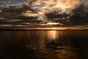 Wall Mural - Glowing sunlight on the cloudy twilight sky is reflected by colorful light and shadows on the lake water