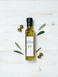 Olive oil glass bottle mock up. Top view of green glass bottle with extra virgin olive oil on white wooden background with green olives and fresh green olive tree leaves. Vertical. Copy space.