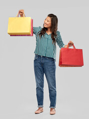 sale, outlet and consumerism concept - happy asian young woman with shopping bags over grey background