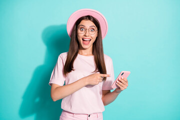 Poster - Photo of impressed girl point finger smartphone wear pink t-shirt sunhat isolated over teal color background