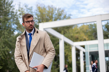 A businessman with glasses leaves the office with a laptop in his hands