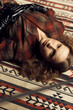 © monchak - stylish curly girl in a vintage checkered jacket, leather gloves lies on the loft studio rug and looks at the camera with a serious expression