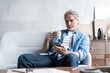 Senior man in couch reading message, using smartphone.