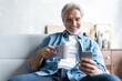 © opolja - Senior man in couch reading message, using smartphone.