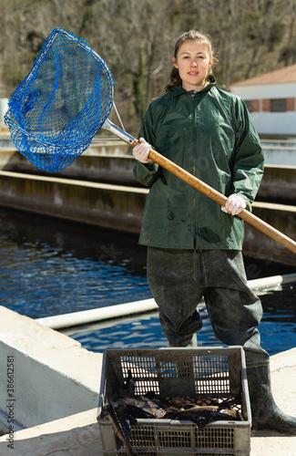 Portrait of woman fish farm worker catching sturgeon at pool