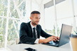 © GVS - Handsome smiling businessman in elegant suit working on laptop in a bright modern office