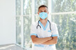 © GVS - Confident male doctor wearing medical mask with arms crossed in hospital background