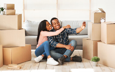 Positive black man and his wife moving to their own apartment together, taking selfie among boxes with belongings