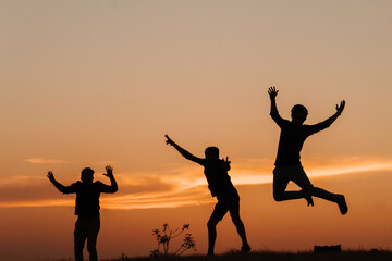 Wall Mural - Silhouette of three Indian friends jumping with arms raised against the sky during the sunset	