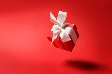 A red gift box with a white bow hangs in the air on a red background with copy space.