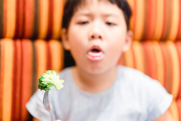 Wall Mural - Little asian girl make vomiting face when she eat broccoli vegetable in restaurant.Unhappy, Disgusted, Unlike veggie food.Little asian girl child with no appetite in front of the meal.Bad behavior.