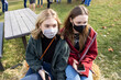 © Mat Hayward - Two teenage girls outside in a park wearing masks on their faces to protect from Covid-19 coronavirus during the pandemic