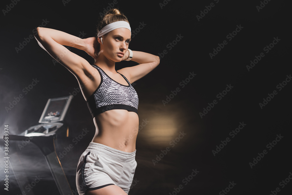 Sportswoman with hands behind head standing near treadmill in gym - obrazy, fototapety, plakaty 