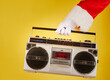 Santa Claus hand holding a radio cassette player on a yellow background