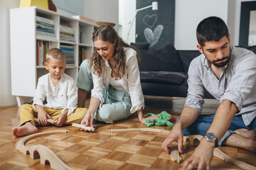 Canvas Print - mother and father playing with their child with wooden train toy at home