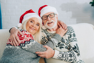 happy senior couple in santa hats embracing while looking at camera