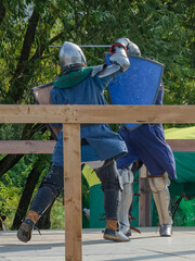 Wall Mural - Two foot warriors in heavy medieval armor fight in the arena. Armed with swords. They are protected by iron helmets and shields. Historical reconstruction of medieval European knightly tournaments