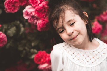 Wall Mural - Pretty smiling baby girl 3-4 year old posing over floral roses background closeup in park. Summer time. Childhood.