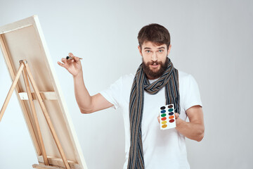 Wall Mural - A man artist paints on an easel a brush and paint in the hands of a hobby creativity light background