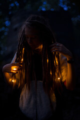 soft focus portrait photography of dreadlocks girl with warm lighting of garland lamps dark vertical picture i night time and background phantom blue bokeh