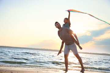 Happy father and his child playing with kite on beach near sea. Spending time in nature